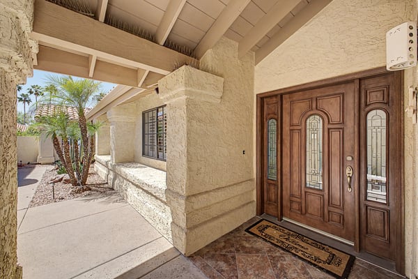 Elegant custom double entry doors create a warm and sophisticated welcome beneath a covered front patio. The gated entry enhances privacy while adding architectural character.