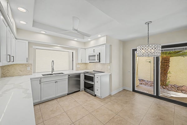 Open kitchen and dining area featuring quartz countertops, white shaker cabinets, stainless steel appliances, designer lighting, and direct access to the private courtyard for seamless indoor-outdoor living.