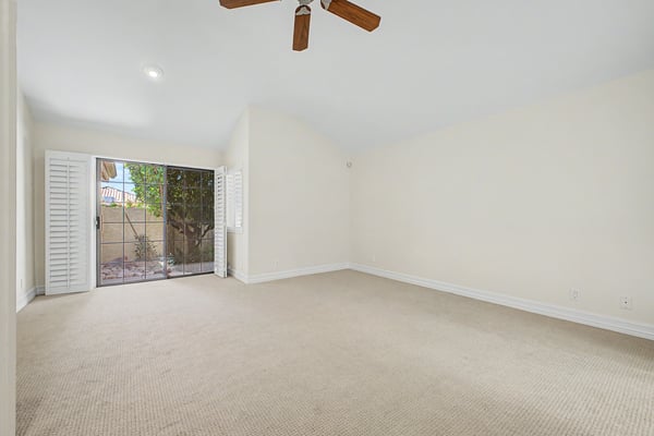 Spacious owner's suite with vaulted ceilings, plush carpet, plantation shutters, and sliding glass doors providing natural light and easy access to the private outdoor patio.