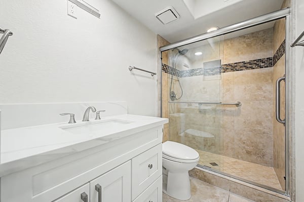 Updated bathroom showcasing a quartz vanity, elegant tiled walk-in shower, glass enclosure, and contemporary fixtures for everyday comfort and convenience.