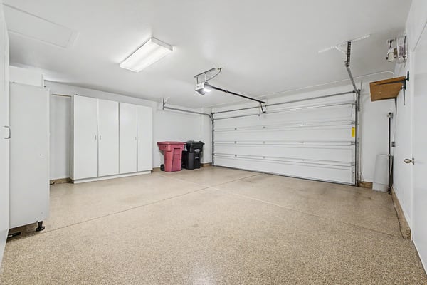 Clean, oversized garage with built-in cabinetry, epoxy-coated flooring, and organized storage solutions, offering functionality beyond vehicle parking.