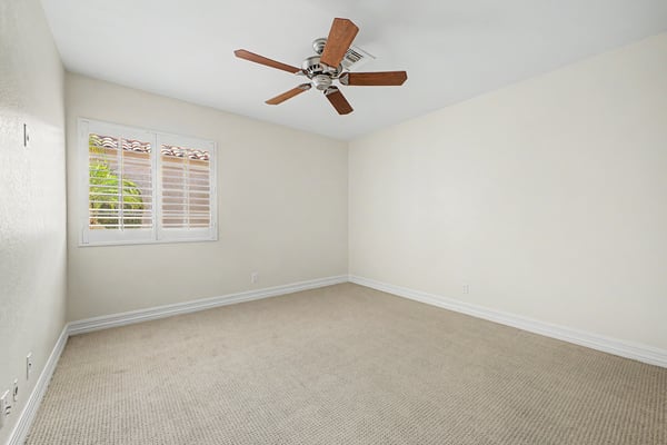 Bright guest bedroom featuring plantation shutters, plush carpeting, ceiling fan, and neutral finishes that easily accommodate family, visitors, or a home office.
