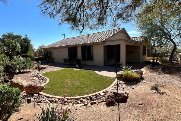 Beautiful backyard showcasing lush artificial turf, paver pathways, decorative rock features, mature desert plants, and tranquil golf course surroundings. A perfect outdoor retreat for relaxing or entertaining guests.