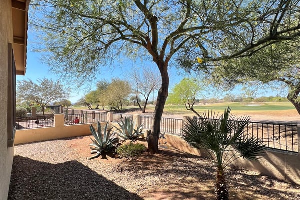 Backyard overlooking the fairway with mature desert trees, attractive landscaping, decorative stone accents, and scenic mountain views. This premium outdoor setting offers both privacy and breathtaking natural surroundings.