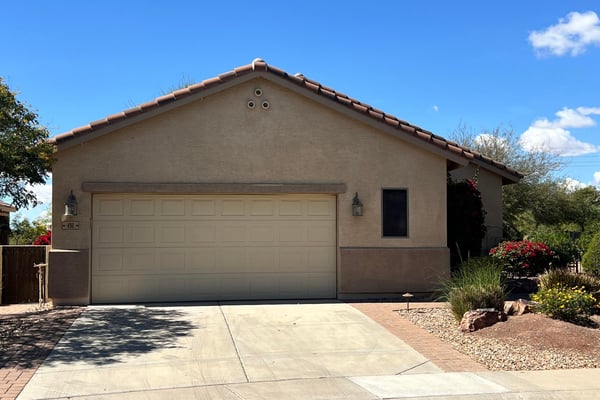 Charming front exterior with mature desert landscaping, spacious driveway, two-car garage, and attractive paver accents creating beautiful curb appeal in a desirable Buckeye neighborhood.