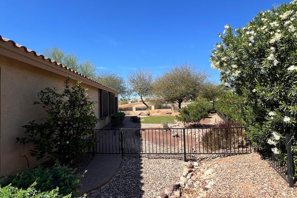 Beautiful side yard featuring flowering shrubs, decorative rock landscaping, gated access, and paver walkways that enhance both privacy and the home's low-maintenance outdoor design.