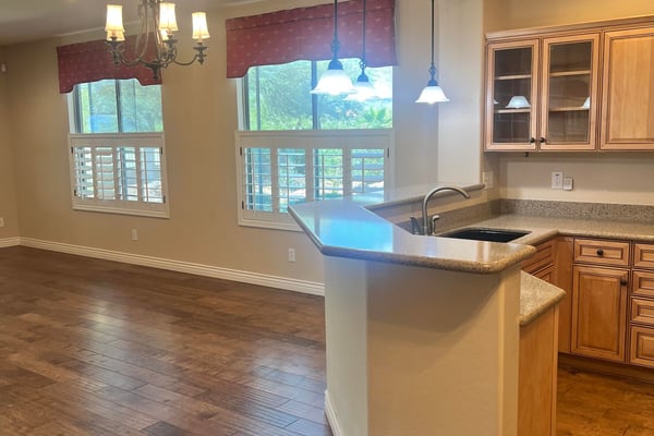 Inviting open-concept kitchen and dining area with custom cabinetry, breakfast bar, pendant lighting, plantation shutters, and upgraded flooring that creates a bright, welcoming atmosphere perfect for entertaining.