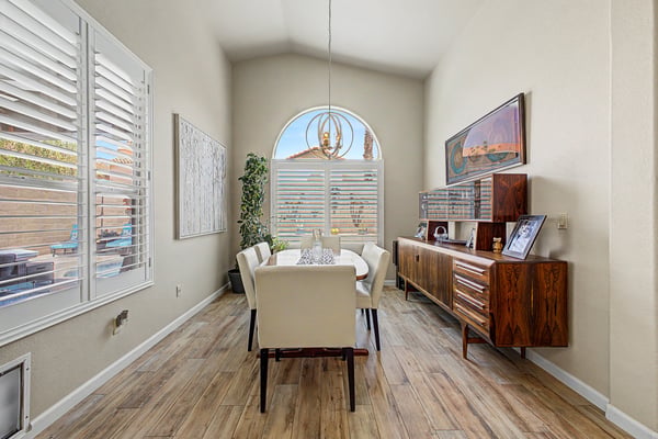 Elegant dining room featuring soaring ceilings, plantation shutters, designer lighting, and beautiful tile flooring. The bright, open atmosphere creates the perfect setting for entertaining family and friends.