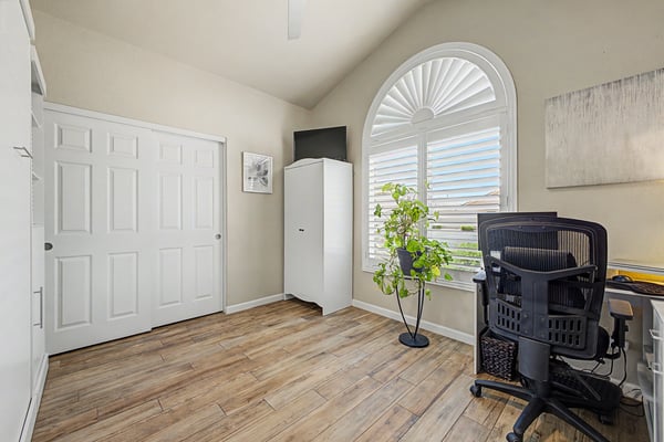Bright secondary bedroom with vaulted ceilings, plantation shutters, tile flooring, and flexible space for guests, a home office, or creative pursuits.