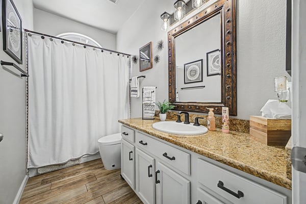 Full guest bathroom showcasing granite countertops, updated hardware, modern lighting, framed mirror, and a convenient tub and shower combination for everyday comfort.