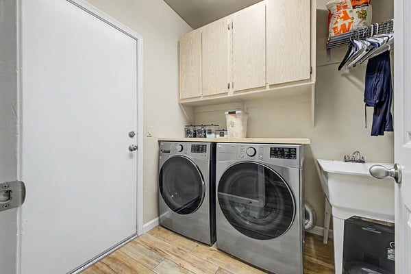 Convenient laundry room equipped with front-load appliances, upper storage cabinets, utility sink, and direct outdoor access. A practical space designed for efficiency.