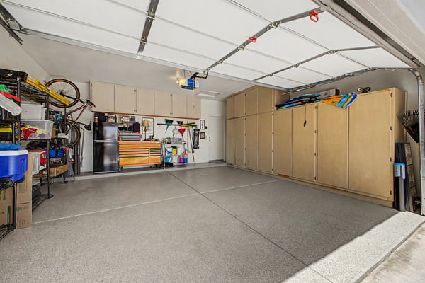 Spacious two-car garage featuring extensive built-in cabinets, epoxy-coated flooring, organized storage, and room for vehicles, tools, and recreational equipment.