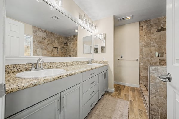 Elegant primary bathroom featuring dual granite countertops, custom cabinetry, upgraded lighting, and a beautifully tiled walk-in shower. A luxurious space thoughtfully designed with premium finishes.