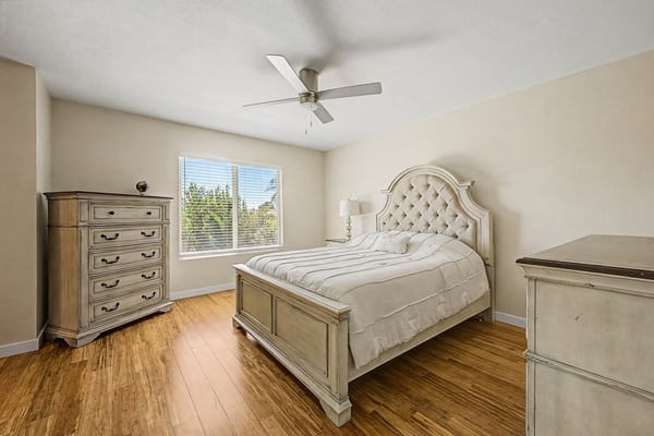 Bright secondary bedroom with wood-look flooring, ceiling fan, large window, and neutral d cor. Perfect for overnight guests, family members, or a dedicated home office.
