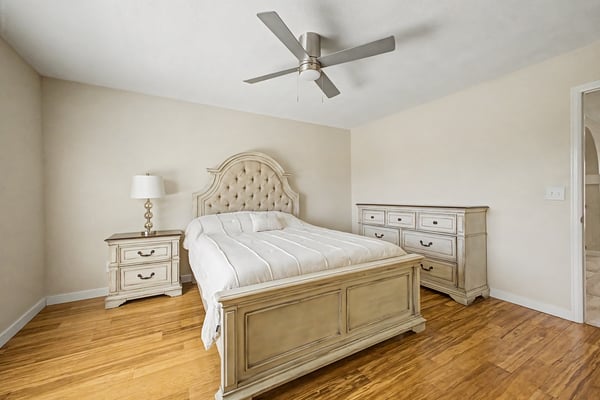 This welcoming bedroom features wood-look flooring, a ceiling fan, generous natural light, and neutral finishes. A versatile space ready to accommodate guests or family.