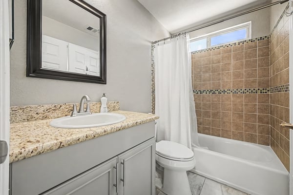 Well-appointed full bathroom featuring granite countertops, decorative tile shower surround, updated cabinetry, and modern finishes. Bright natural light enhances this welcoming Scottsdale space.
