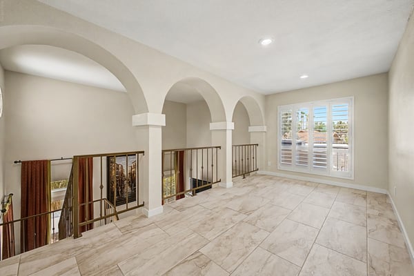 Expansive loft with elegant arches, iron railings, upgraded tile flooring, and an open layout overlooking the main level. A versatile gathering space in this Scottsdale home.
