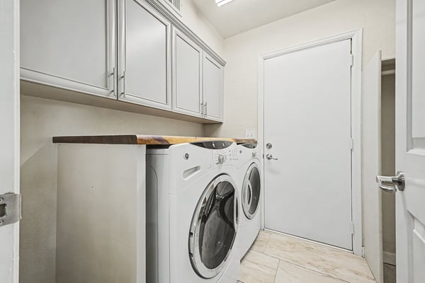 Convenient laundry room with overhead cabinetry, countertop workspace, tile flooring, and space for full-size washer and dryer. Functional storage enhances daily living.