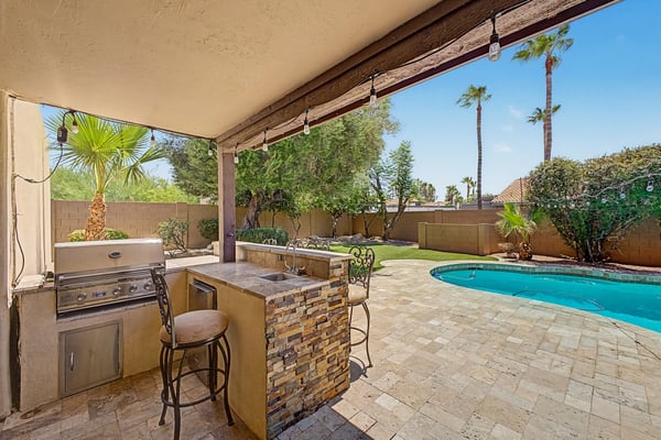 Outdoor entertaining space with a built-in BBQ grill, prep sink, bar seating, covered patio, and views of the sparkling pool. A beautifully designed Scottsdale backyard made for gatherings and outdoor dining.
