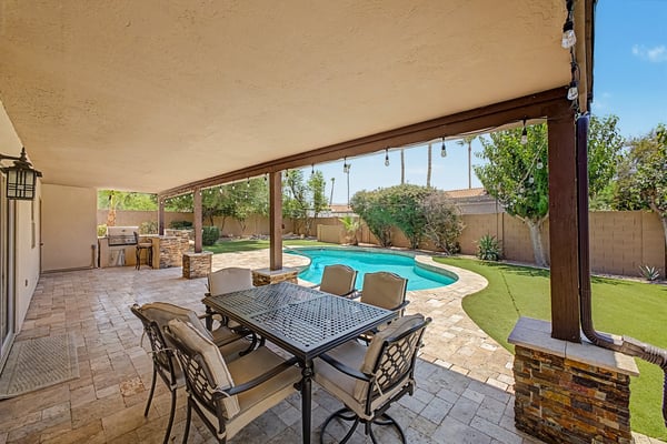 Covered patio with comfortable outdoor dining space, travertine flooring, decorative lighting, and peaceful views of the pool and landscaped yard. Enjoy year-round Scottsdale outdoor living.