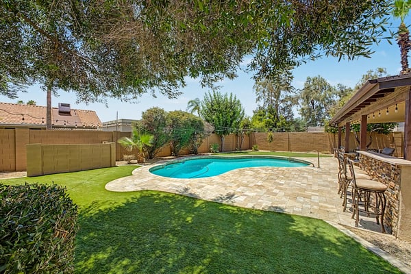 Exceptional outdoor living area featuring a sparkling pool, travertine patio, built-in BBQ kitchen, bar seating, and beautifully landscaped grounds. This Scottsdale backyard combines comfort, style, and functionality for year-round enjoyment.