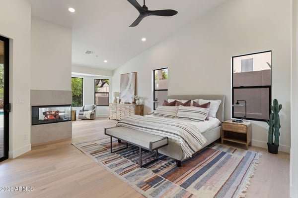 Spacious owner's suite with soaring ceilings, a contemporary fireplace, sitting area, and beautiful backyard views. Thoughtfully designed for luxury, comfort, and everyday living in this Scottsdale home.