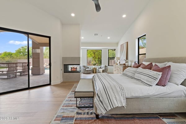 Beautiful primary bedroom featuring a fireplace, comfortable sitting area, large sliding glass doors, and peaceful backyard views. This luxurious Scottsdale retreat offers a relaxing atmosphere with elegant finishes and direct access to the outdoor living spaces.