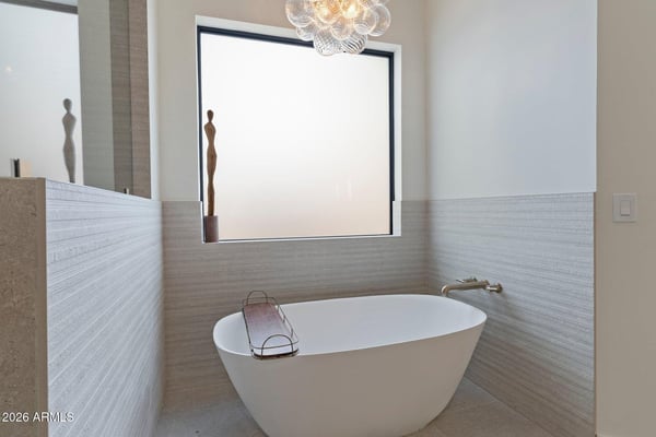 Elegant soaking tub surrounded by designer tile, oversized window, and modern lighting. A peaceful retreat designed for comfort and relaxation within the luxurious primary suite.