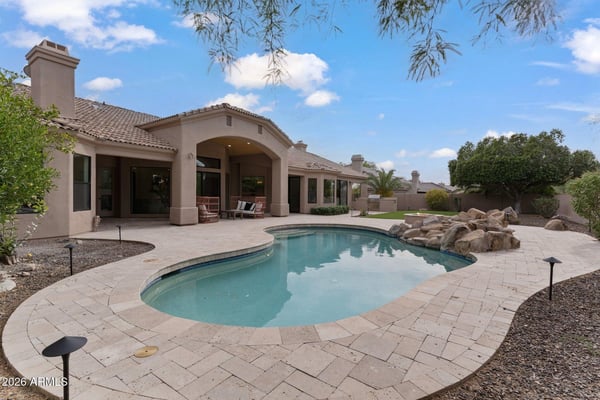 Beautiful outdoor living space featuring a sparkling swimming pool, expansive paver patio, artificial turf, mature landscaping, and generous entertaining areas in this Scottsdale home.