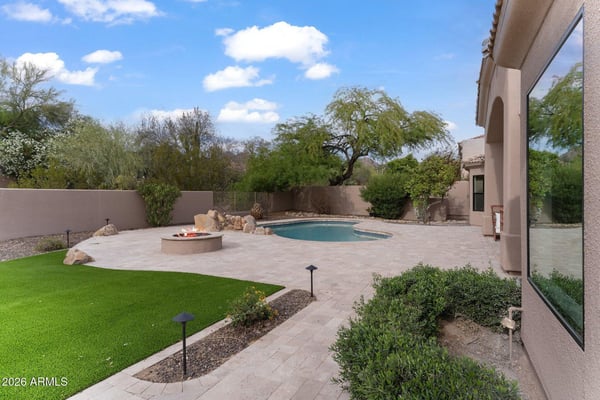 Private Scottsdale backyard featuring a sparkling swimming pool, custom fire pit, expansive paver patio, artificial turf, and mature landscaping designed for relaxing and entertaining.