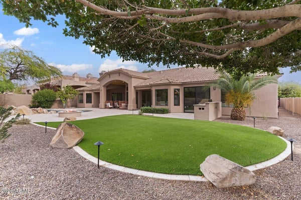 Resort-inspired backyard with a covered patio, sparkling pool, outdoor kitchen, artificial lawn, and generous entertaining space. A beautiful extension of this Scottsdale home's luxury living.