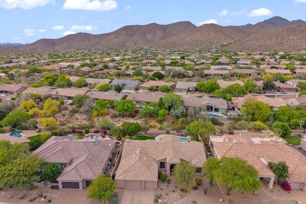 Sweeping aerial perspective capturing the Scottsdale neighborhood, nearby mountain scenery, mature desert landscaping, and the home's desirable residential setting.