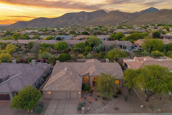 Beautiful sunset aerial featuring the home's attractive exterior framed by breathtaking mountain views and mature desert landscaping. This Scottsdale residence offers an exceptional setting with outstanding curb appeal.