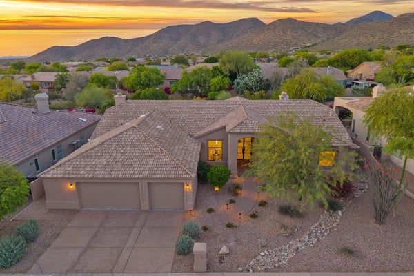 Twilight aerial showcasing the welcoming front elevation, spacious three-car garage, and professionally landscaped front yard. Located in a sought-after Scottsdale neighborhood with scenic mountain views.