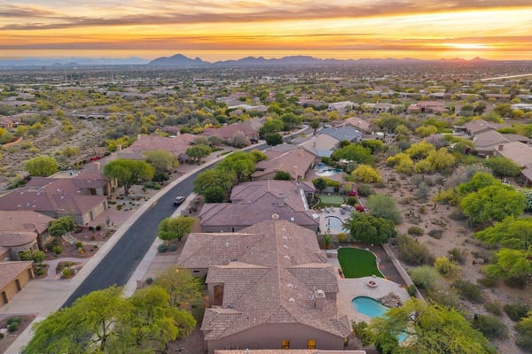 Expansive aerial capturing the surrounding Scottsdale neighborhood, dramatic mountain scenery, nearby desert wash, and the home's desirable location among beautifully maintained luxury residences.
