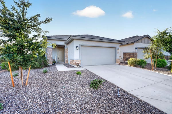 The welcoming front entry is complemented by attractive desert landscaping, mature greenery, stone accents, and a spacious driveway, creating a polished first impression of this Surprise property.