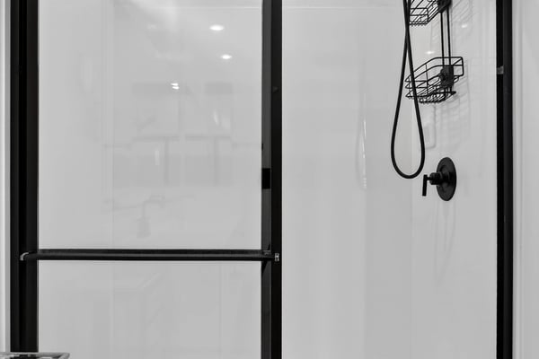 The oversized walk-in shower features sleek glass doors, contemporary black fixtures, built-in storage shelves, and a low-maintenance design that enhances the spa-like feel of the primary bath.