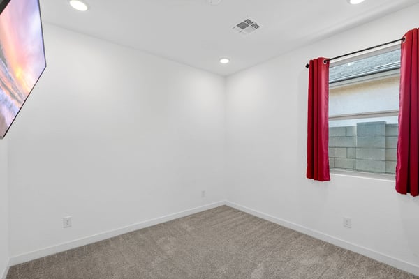 A bright guest bedroom with plush carpet, recessed lighting, and a large window provides comfortable accommodations while complementing the home's open and modern design.
