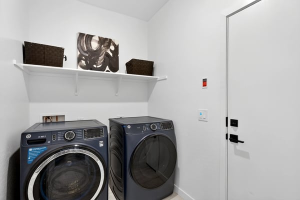 Designed for convenience, this laundry room includes upper shelving, modern appliances, and direct garage access to simplify everyday routines while maximizing storage.