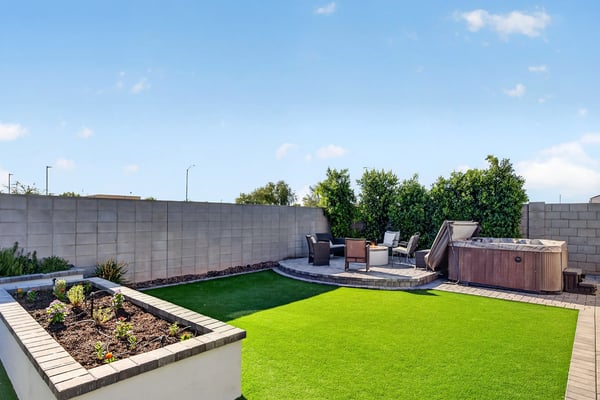 Beautiful backyard featuring artificial turf, raised garden planters, paver hardscaping, and a private hot tub creates a low-maintenance outdoor oasis in Surprise.