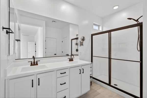 This well-appointed primary bathroom showcases dual sinks, quartz counters, modern cabinetry, black fixtures, and a spacious walk-in shower for a clean contemporary design.