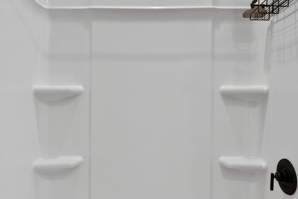 This updated bathroom includes a spacious tub and shower combination with contemporary matte black fixtures, built-in storage shelves, and low-maintenance finishes.