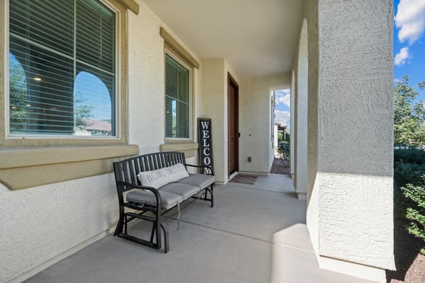 Inviting front entrance featuring a spacious covered patio, decorative columns, and comfortable seating area. Thoughtfully designed to provide shade and curb appeal year-round.
