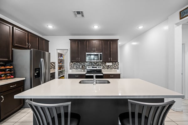 Large quartz island with integrated sink and breakfast bar seating anchors this beautifully appointed kitchen. Rich cabinetry, stainless steel appliances, and a walk-in pantry complete the space.