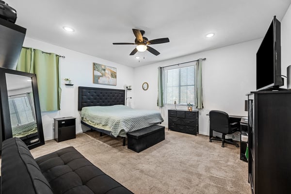 Spacious primary suite with plush carpeting, ceiling fan, generous natural light, and room for additional seating or workspace. A relaxing retreat designed for comfort and privacy in this beautiful Goodyear home.