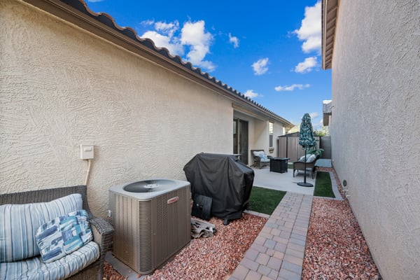 Side yard featuring paver walkways, decorative rock landscaping, artificial turf, and outdoor grilling space. Designed for beauty, functionality, and low-maintenance living.