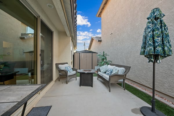 Covered backyard patio with comfortable seating, a fire table, artificial turf, and additional storage. A welcoming outdoor retreat perfect for relaxing or entertaining guests.