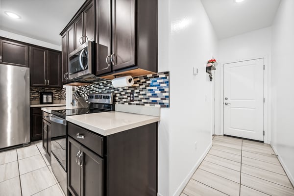 Well-designed kitchen with direct garage entry, modern cabinetry, quartz counters, stainless steel appliances, and decorative backsplash. Convenience and style come together beautifully.