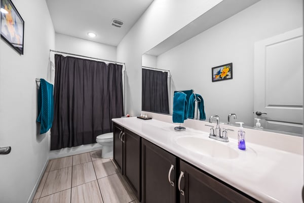 Spacious guest bathroom with an extended vanity, tub and shower combination, and contemporary finishes. Designed to comfortably serve family members and visitors alike.