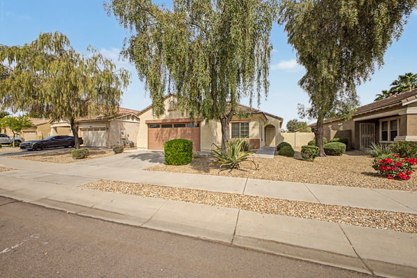 Beautiful front streetscape featuring established shade trees, desert landscaping, and a well-maintained exterior that complements this inviting Palm Valley home.